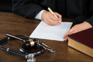 Judge Writing On Document With Mallet And Stethoscope At Desk